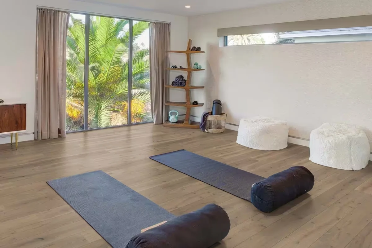 Bright room with a light brown oak-look engineered wood floor, two yoga mats and tall windows facing palm trees
